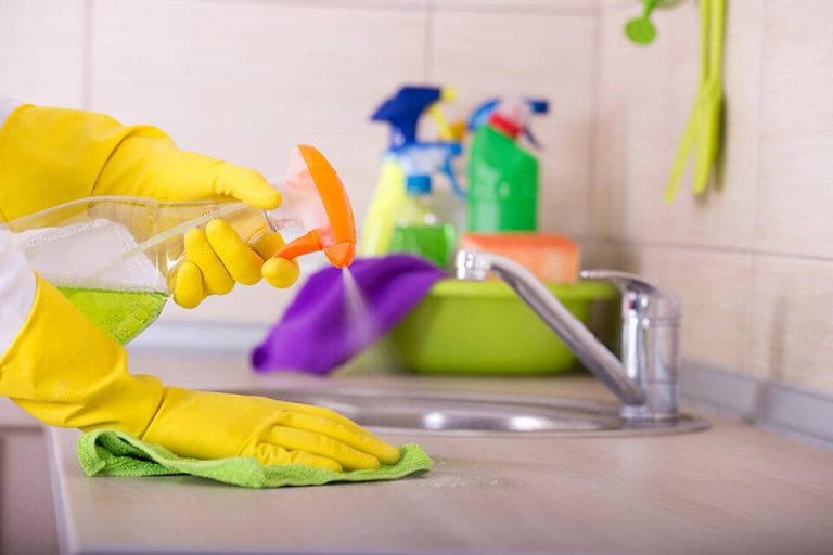 Hands wearing rubber gloves cleaning sink with cleaner